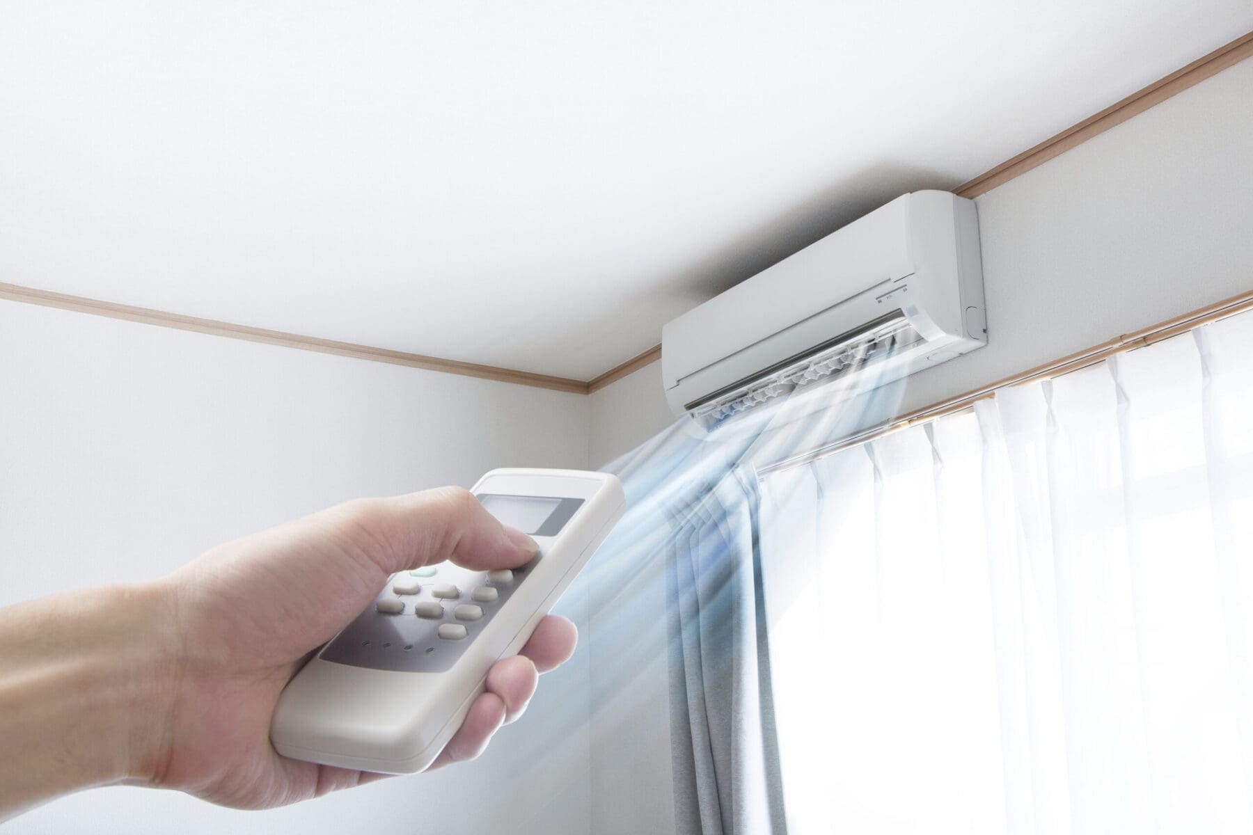 Hand pointing at a ductless mini-split with a remote to turn the unit on