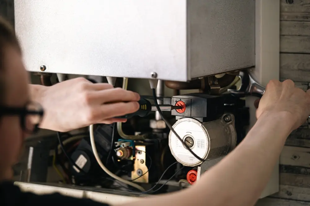 Man is repairing a heating boiler, a screwdriver and a spanner in his hands.