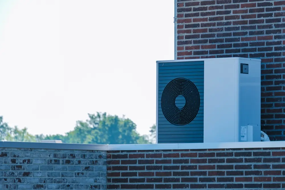 An air source heat pump rests on the rooftop of a contemporary structure, harnessing natural energy under a clear blue sky.